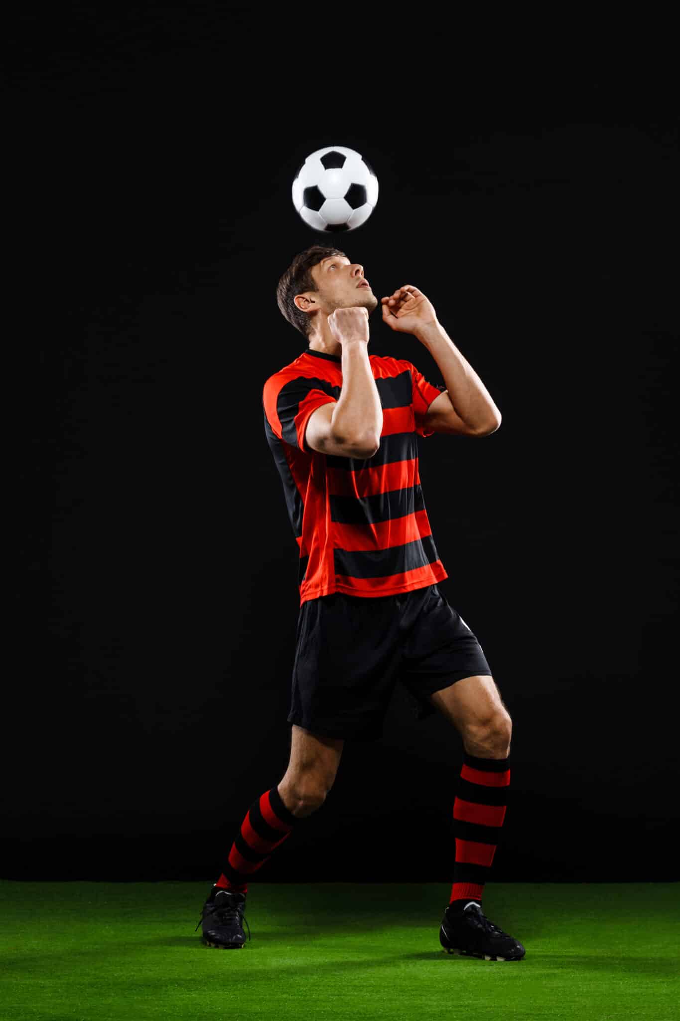 Joueur de football en tenue noire et rouge jonglant avec un ballon sur fond noir.