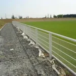 Installation de main courante le long d'un terrain de sport avec un chemin de gravier.